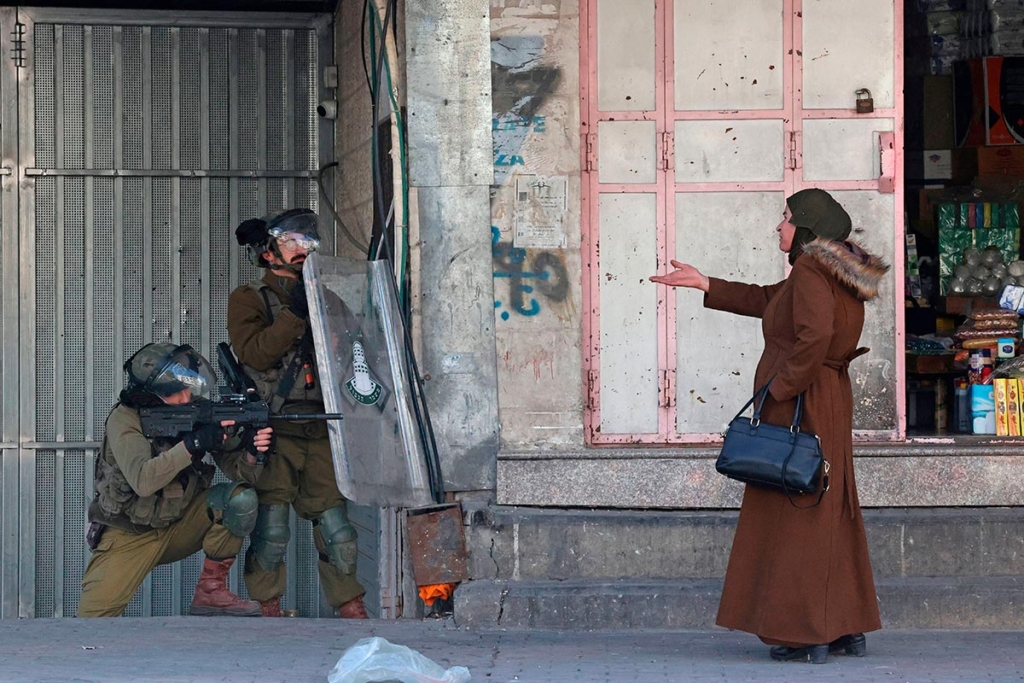 En kvinde står foran de israelske sikkerhedsstyrker, der affyrer gummikugler for at sprede palæstinensiske stenkastere midt i sammenstød i byen Hebron på Vestbredden den 9. februar 2022.